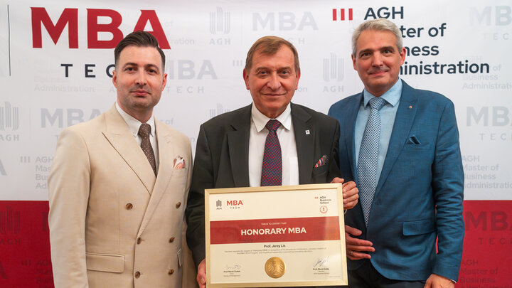 Image of Professor Murat Colak, Professor Jerzy Lis, and Professor Marek Dudek standing in front of a photo wall with the logo of MBA Tech and the AGH University. Professor Lis pictured holding a framed honorary MBA degree