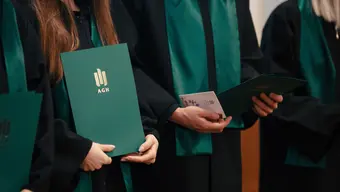 Sillhouettes of graduates in black gowns with dark green shawls. One student is holding a green folder with the AGH University golden logo.