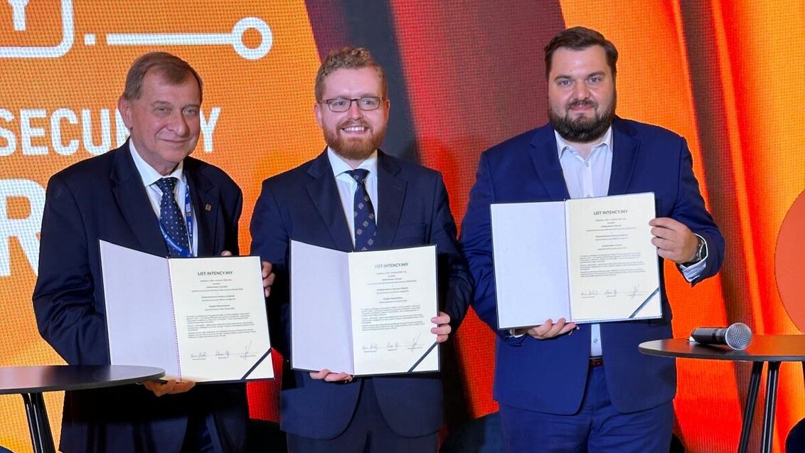 Image of three standing man holding folders with signed agreements in front of a colorful screen