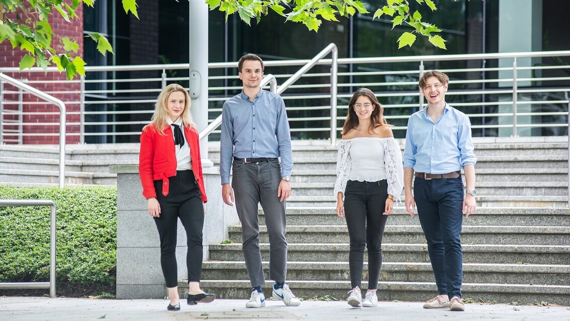 Image of four students, 2 girls and 2 boys, standing outside in front of stairs