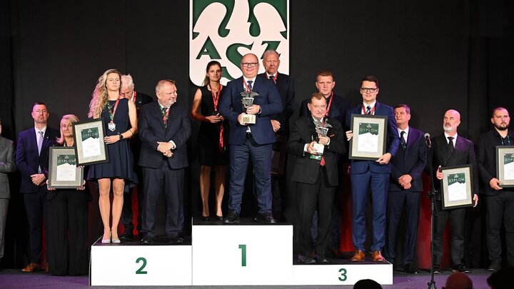 Image of a large group of people standing on a podium. Each step of the podium is occupied by a different team holding awards. The logo of the Academic Sports Association hangs on the wall.