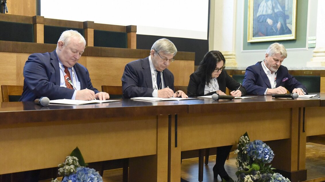 Image of four people simultaneously signing documents in business attire