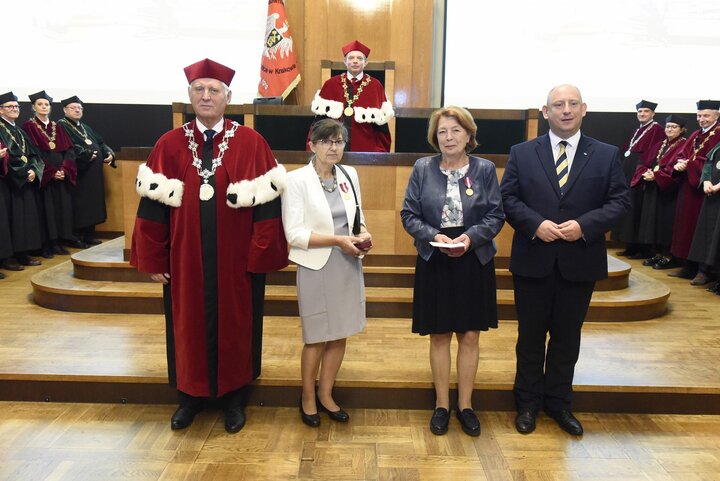 A formal group photo with people in business attire and a man in a red academic robe. They stand in front of a group of university authorities during an award ceremony in the formal AGH University Assembly Hall.