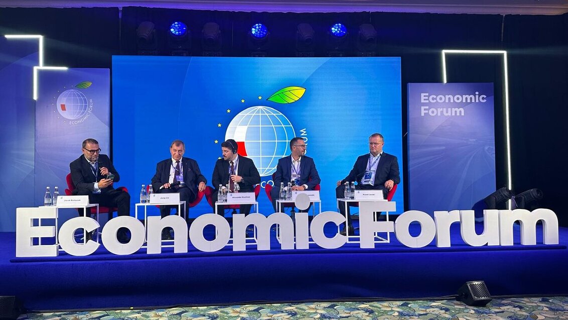 Image of a discussion panel, five panellists sitting on stage in front of blue backdrops, large white letters saying "Economic Forum" are placed in front of the stage