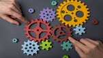 Image of a person touching colorful gear wheels with their index fingers