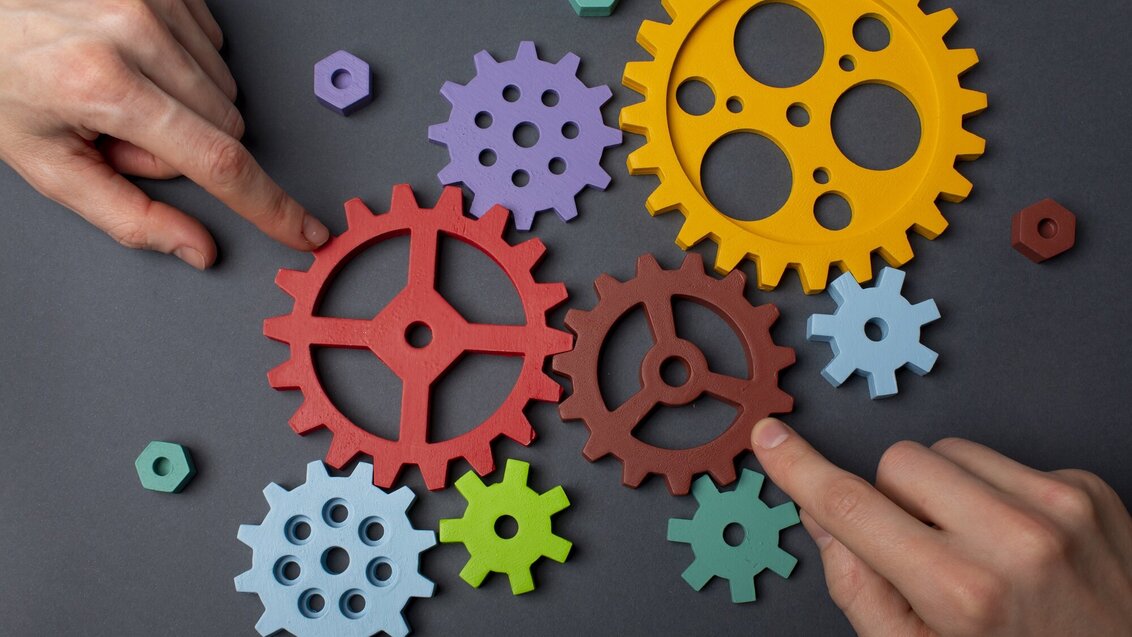 Image of a person touching colorful gear wheels with their index fingers