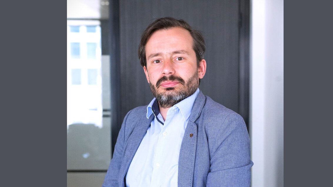 Image of a bearded man wearing a light-blue shirt a a blue jacket