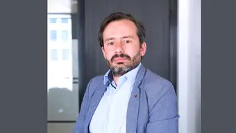 Image of a bearded man wearing a light-blue shirt a a blue jacket