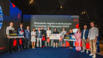 Grupowe zdjęcie laureatów konkursu. Kilkoro z nich trzyma plansze z informacją o zajętym miejscu i wysokości nagrody.