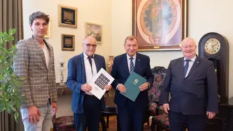 Image of 4 men standing in a study, two of them standing in the middle hold folders, all of them pose for the photo and smile; the men are: Prof. Jerzy Lis, Prof. Rafał Wiśniowski, Krzysztof Smolarski, and Piotr Smolarski.