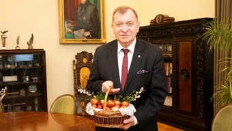Professor Jerzy Lis in a black suit holding an Easter basket filled with eggs in his office.
