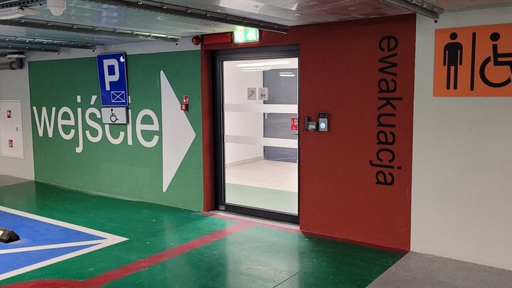 Image of the entrance to the building from the underground car park. The entrance is clearly marked with green and a large sign. There is a symbol of a person in wheelchair on the wall.