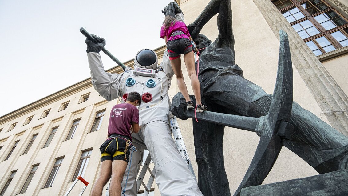 Image of monuments in front of the main building of the AGH University, two mountain climbers dressing a miner's monument as an astronaut