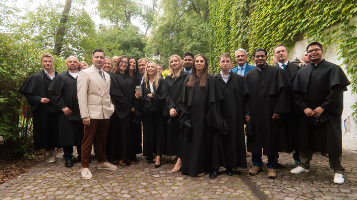 Image of students wearing black graduation gowns pictured with Professor Colak