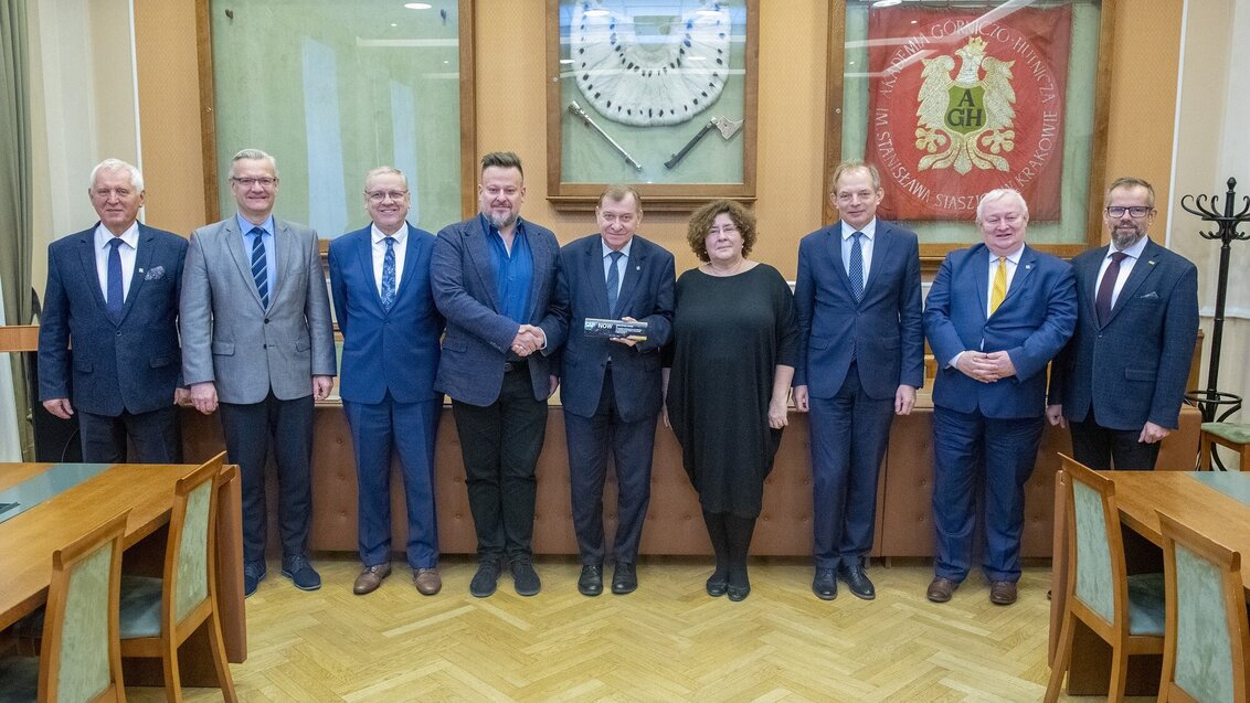 Image of a group of people, mostly men and one woman - the main AGH University authorities, standing in line. The Rector is shaking hands with Grzegorz Król standing on his right-hand side.