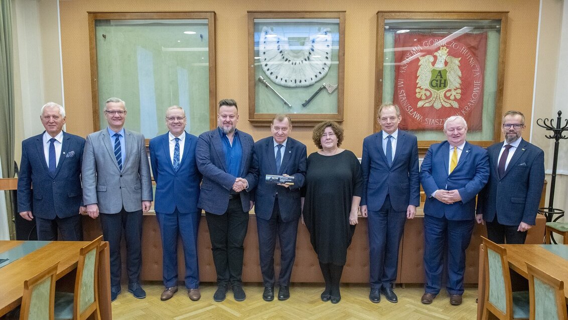 Na zdjęciu dziewięć osób (w tym Rektor i Prorektorzy). Stoją obok siebie w sali konferencyjnej. Rektor trzyma w ręku statuetkę nagrody.