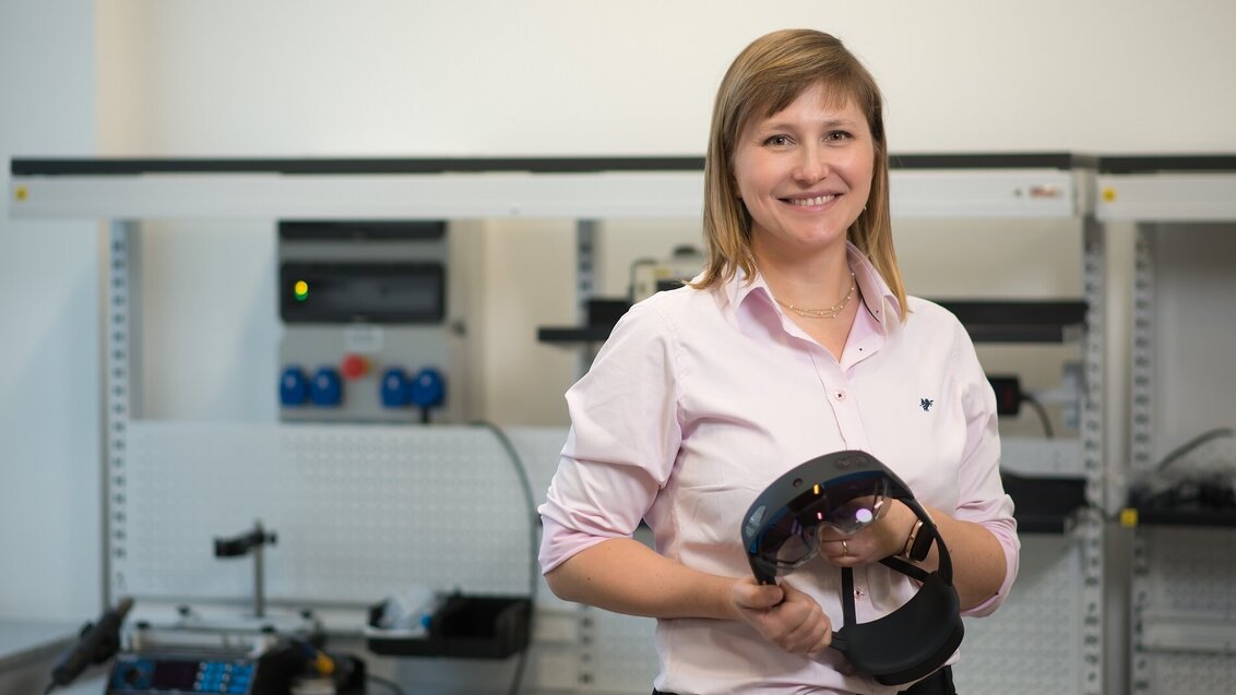 Image of Dr Daria Hemmerling standing in a laboratory holding VR googles