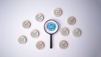 magnifying glass hovers over a blue document icon with a white checkmark, surrounded by wooden tokens each marked with green checkmarks.