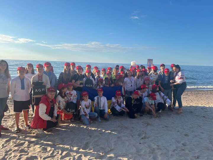 Grupowe zdjęcie dzieci z opiekunami wykonane w słoneczny dzień na plaży.