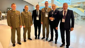 The image shows six men, one of them being the AGH University Rector, three in military uniforms and in business suits, standing together in a modern conference space. They're wearing event badges.