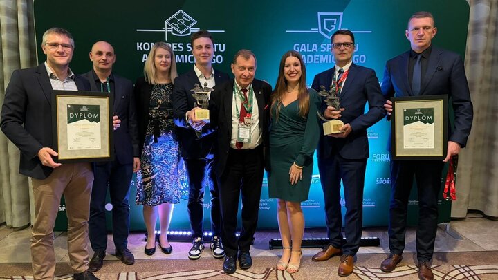 Image of a group of people standing in front of a green backdrop with five of them presenting awards