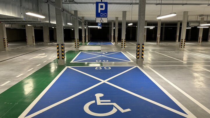 The image shows underground parking spaces reserved for individuals with disabilities. The spaces are marked with large blue rectangles featuring the white wheelchair symbol. There is also a sign overhead with the same symbol, clearly indicating accessibility. The area is well-lit, with columns separating parking spots.