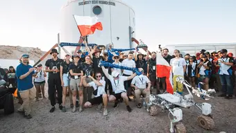 Image of the Polish team posing for a photo with Kalman, their rover, standing in the front. Two people are waving Polish flags