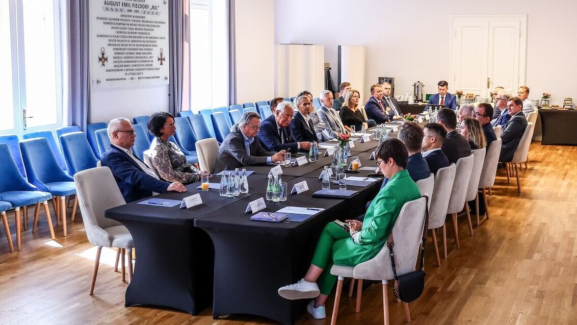 Image of a conference room with a large table in the middle and with a group of people sitting and talking