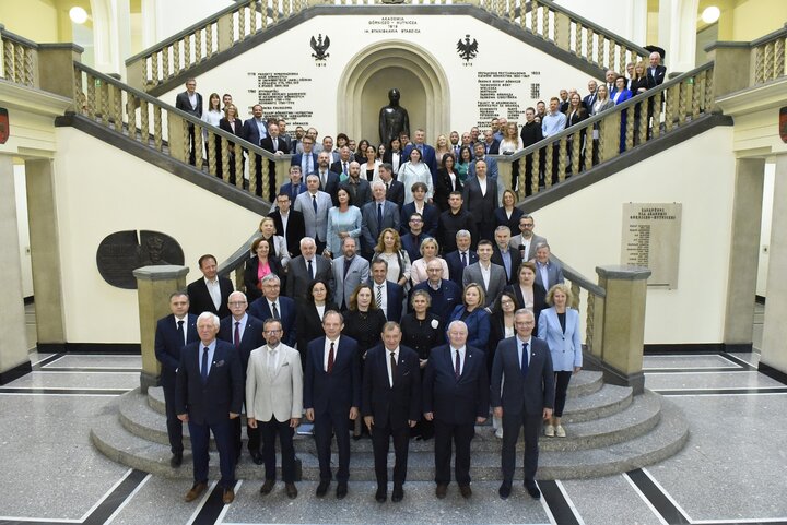 Image of a large group of people standing on a staircase in the AGH University main hall; among the people are university authorities, representatives of faculties, units, and students