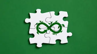 Kolorowa grafika ilustracyjna: cztery połączone ze sobą białe puzzle na zielonym tle; na puzzlach rysunek przewróconej ósemki (w poziomie) ze strzałką i listkami, jako symbol gospodarki o obiegu zamkniętym.