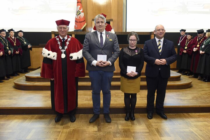 A formal group photo with people in business attire and a man in a red academic robe. They stand in front of a group of university authorities during an award ceremony in the formal AGH University Assembly Hall.