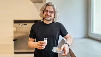 Image of a man in a black t-shirt holding a small beaker of milk in one hand and test samples in the other