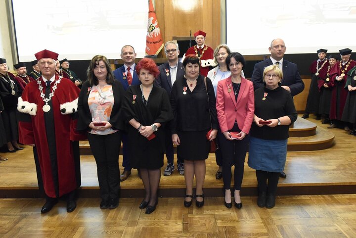 A formal group photo with people in business attire and a man in a red academic robe. They stand in front of a group of university authorities during an award ceremony in the formal AGH University Assembly Hall.