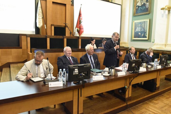 Image of AGH University rectors sitting at the presidential table in the AGH University assembly hall; the AGH University rector is holding a microphone, speaking; two more people sitting on the right-hand side