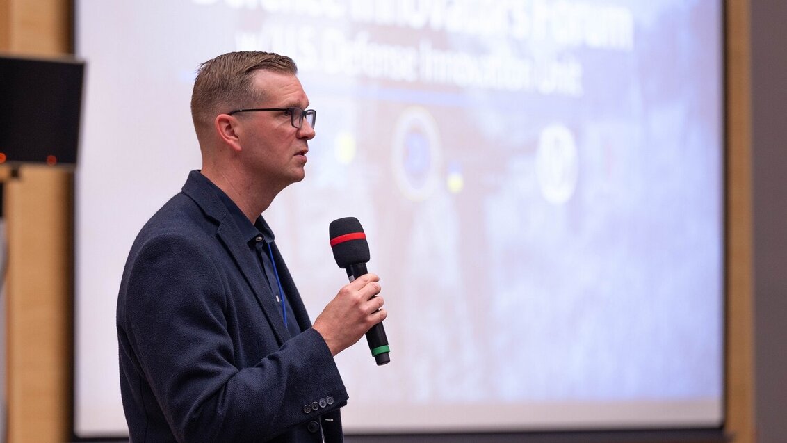 Photo of a man delivering a speech in front of a screen