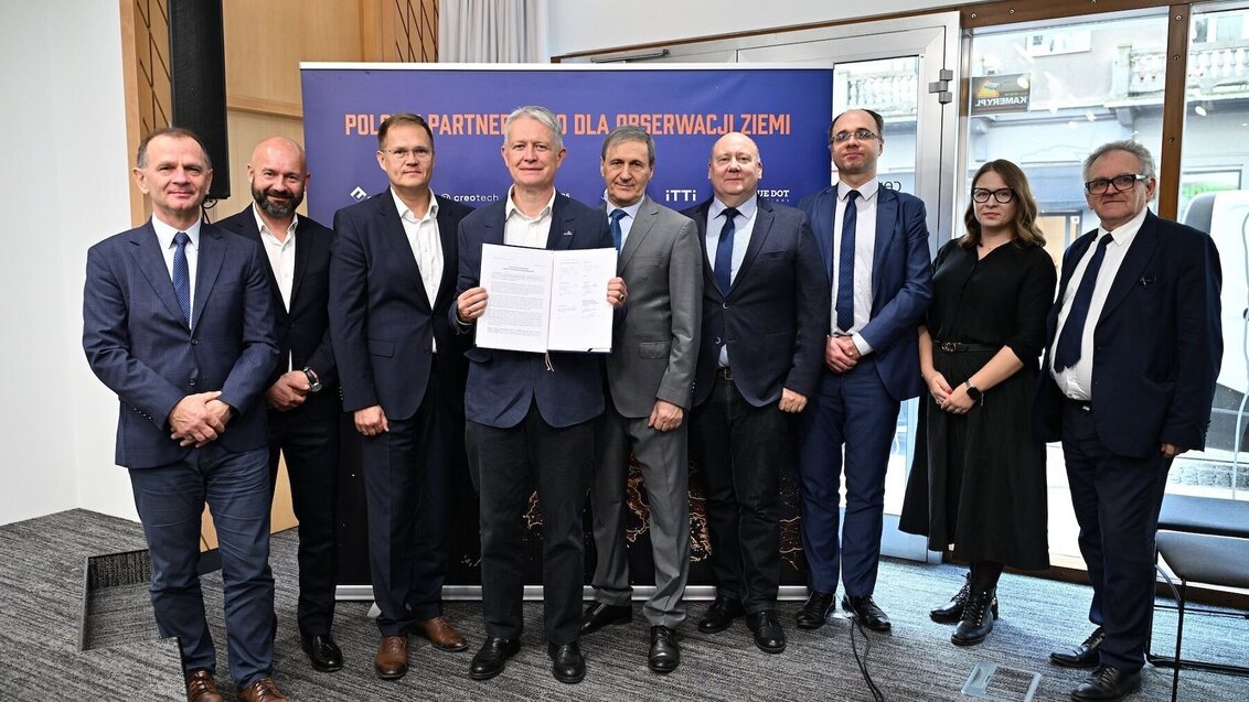 Image of a group of people in business attire, probably after signing an agreement, as one of the people is holding a folder with a signed document