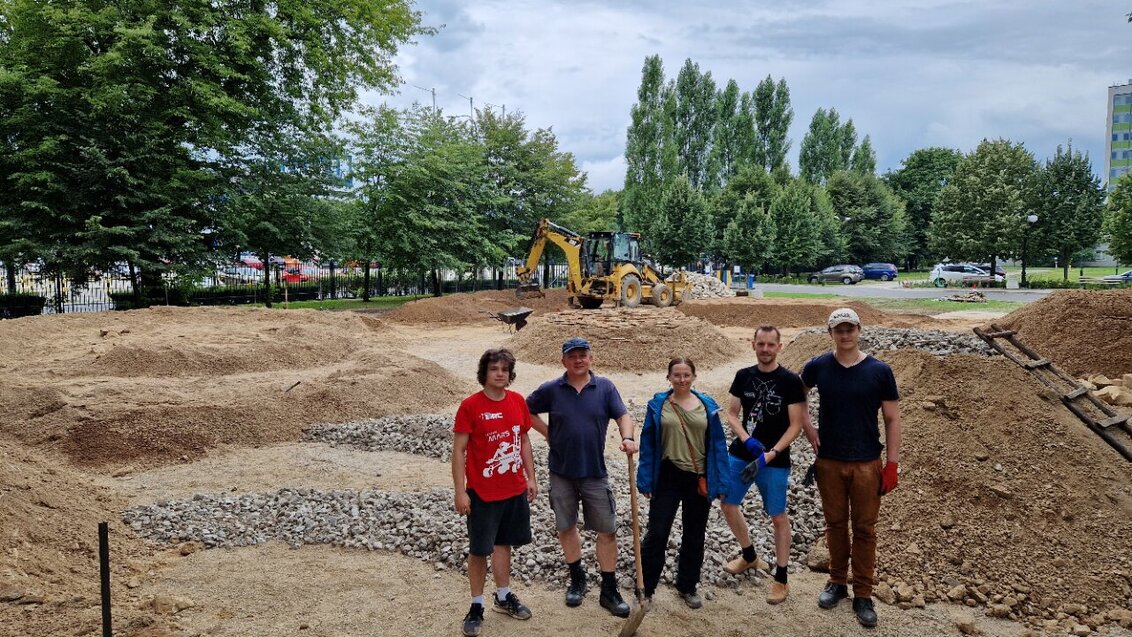 Image of a group of people standing in front of a track which is supposed to imitate the surface of Mars, some greenery isible in the background