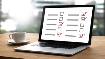 A decorative image of a laptop and a coffee cup on a wooden desk. The laptop screen displays a list with checkboxes. Some are marked with red ticks.